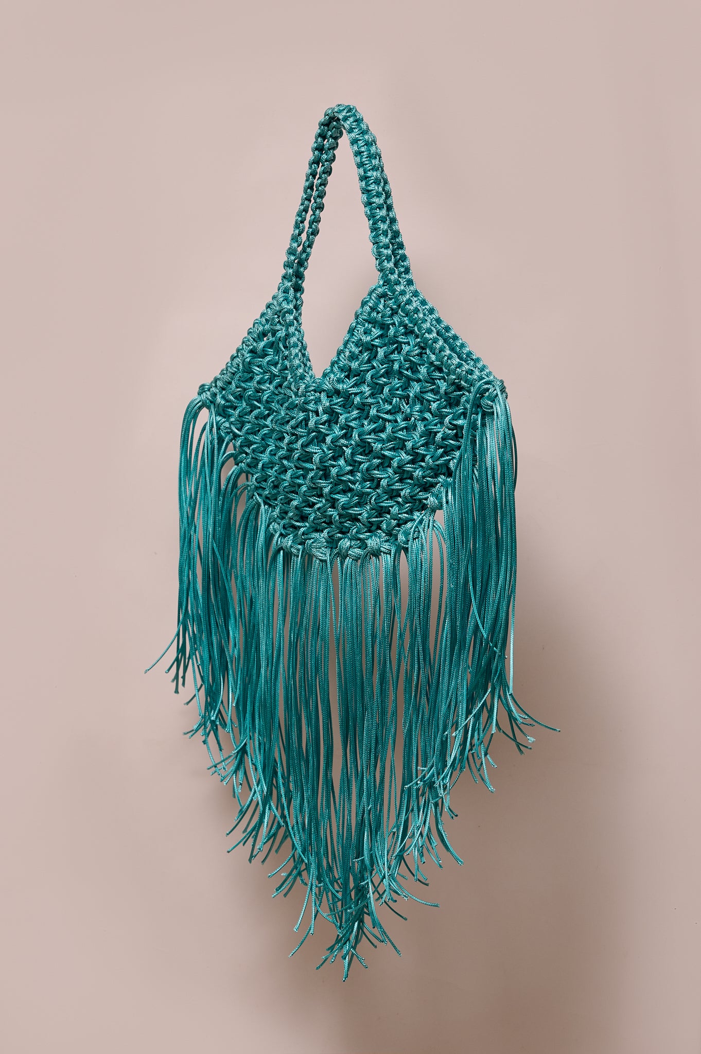 Teal macrame bag with fringes on a beige background