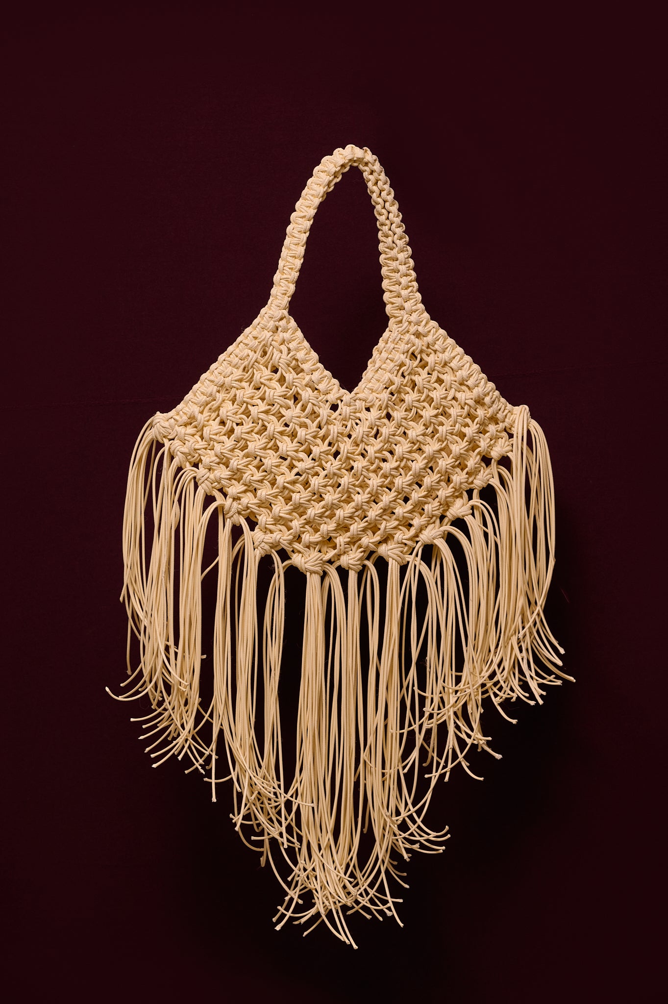 Ivory woven handbag with fringe on a burgundy background