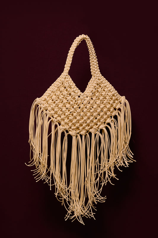 Ivory woven handbag with fringe on a burgundy background
