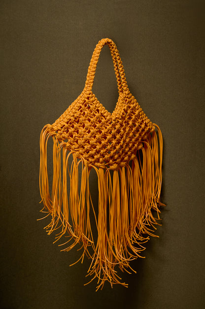 Yellow mustard woven bag with fringes on a dark oilvebackground