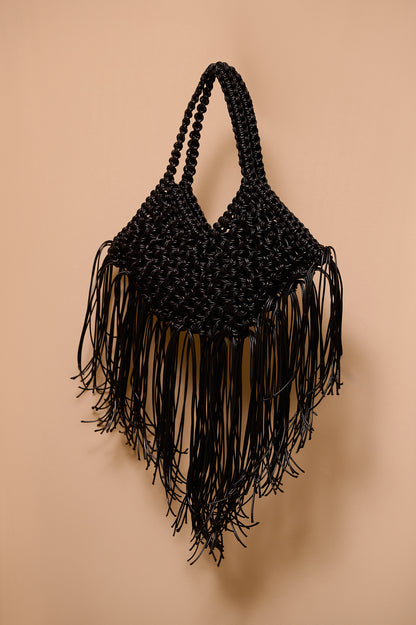 Black woven handbag with fringe on a beige background