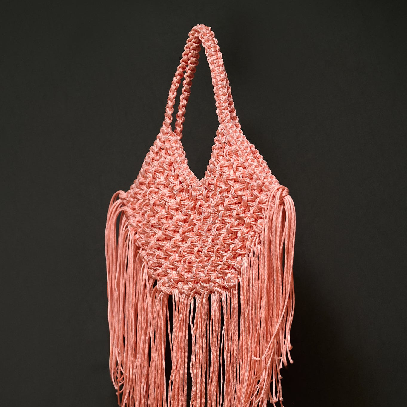 Pink woven handbag with fringe on a black background
