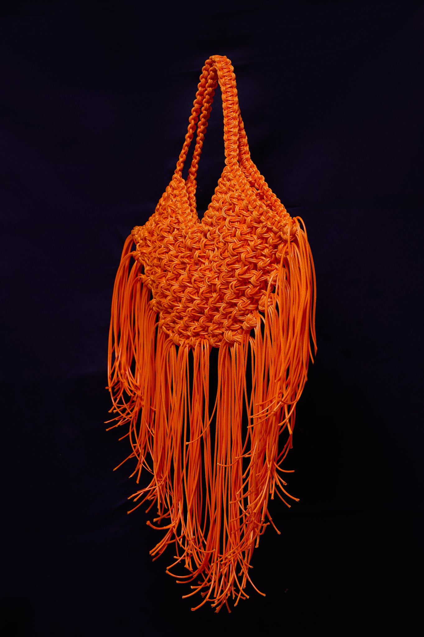 Orange woven handbag with fringes on a black background