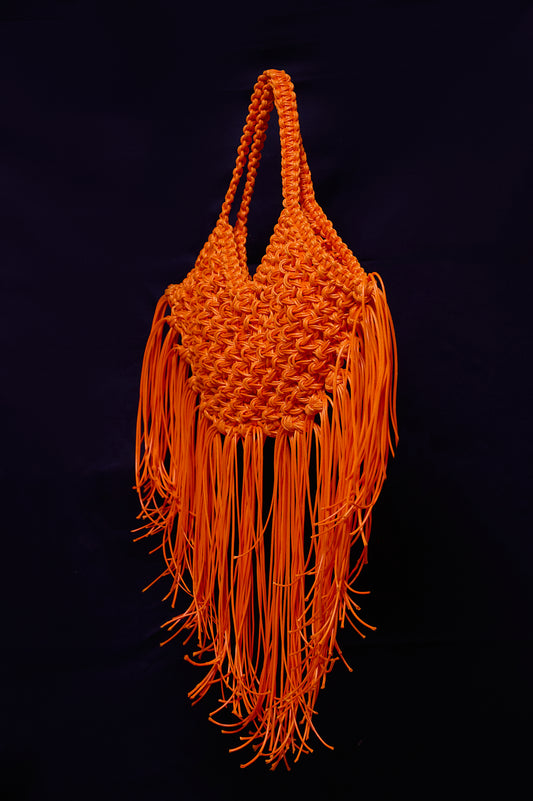 Orange woven handbag with fringes on a black background