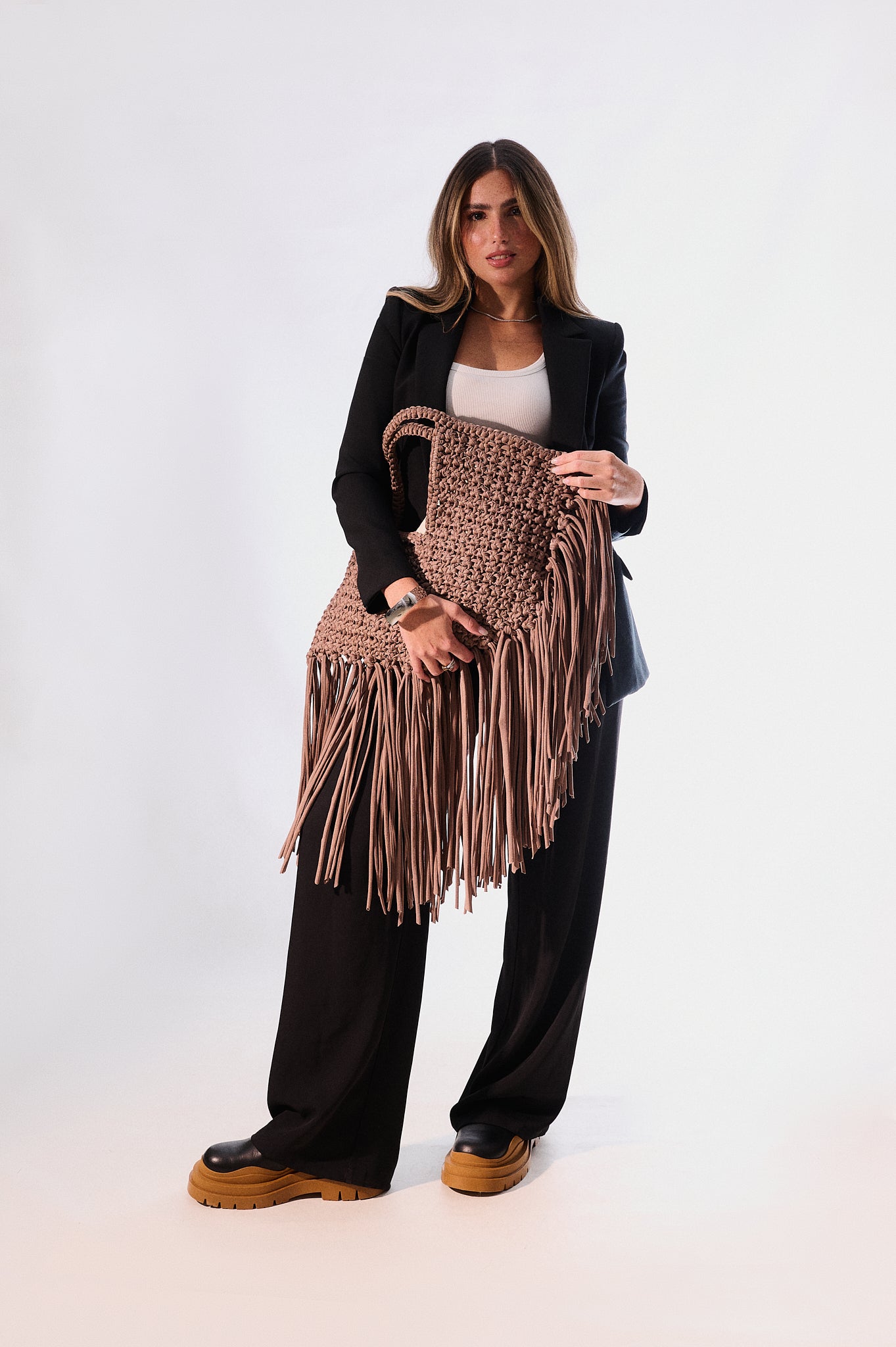Woman holding a brown fringed bag against a white background